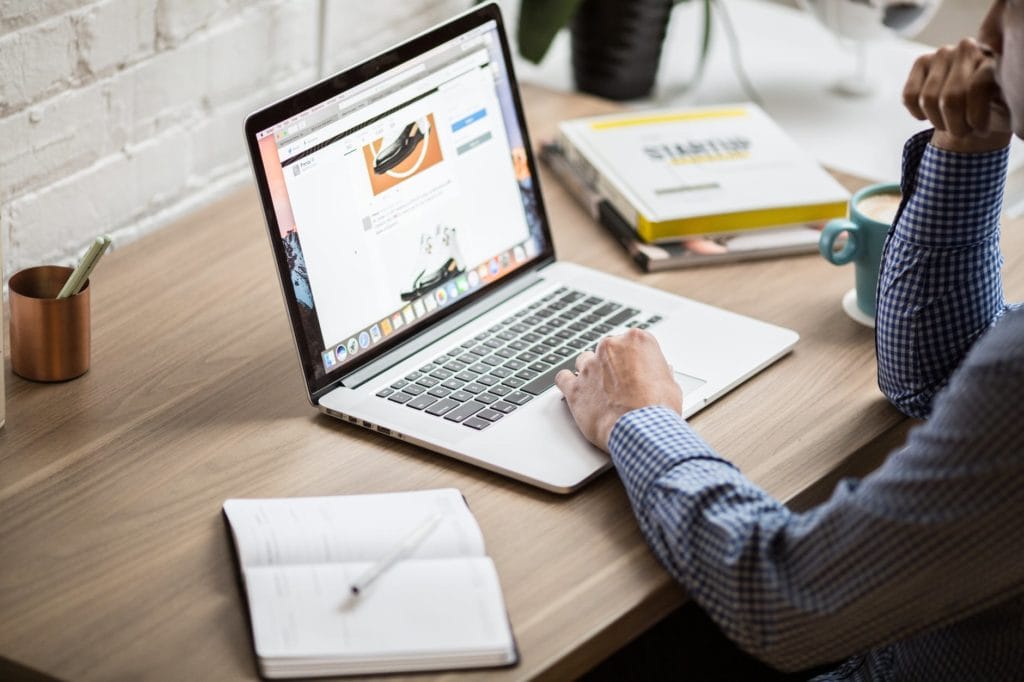 A man scrolling on his laptop at his desk.