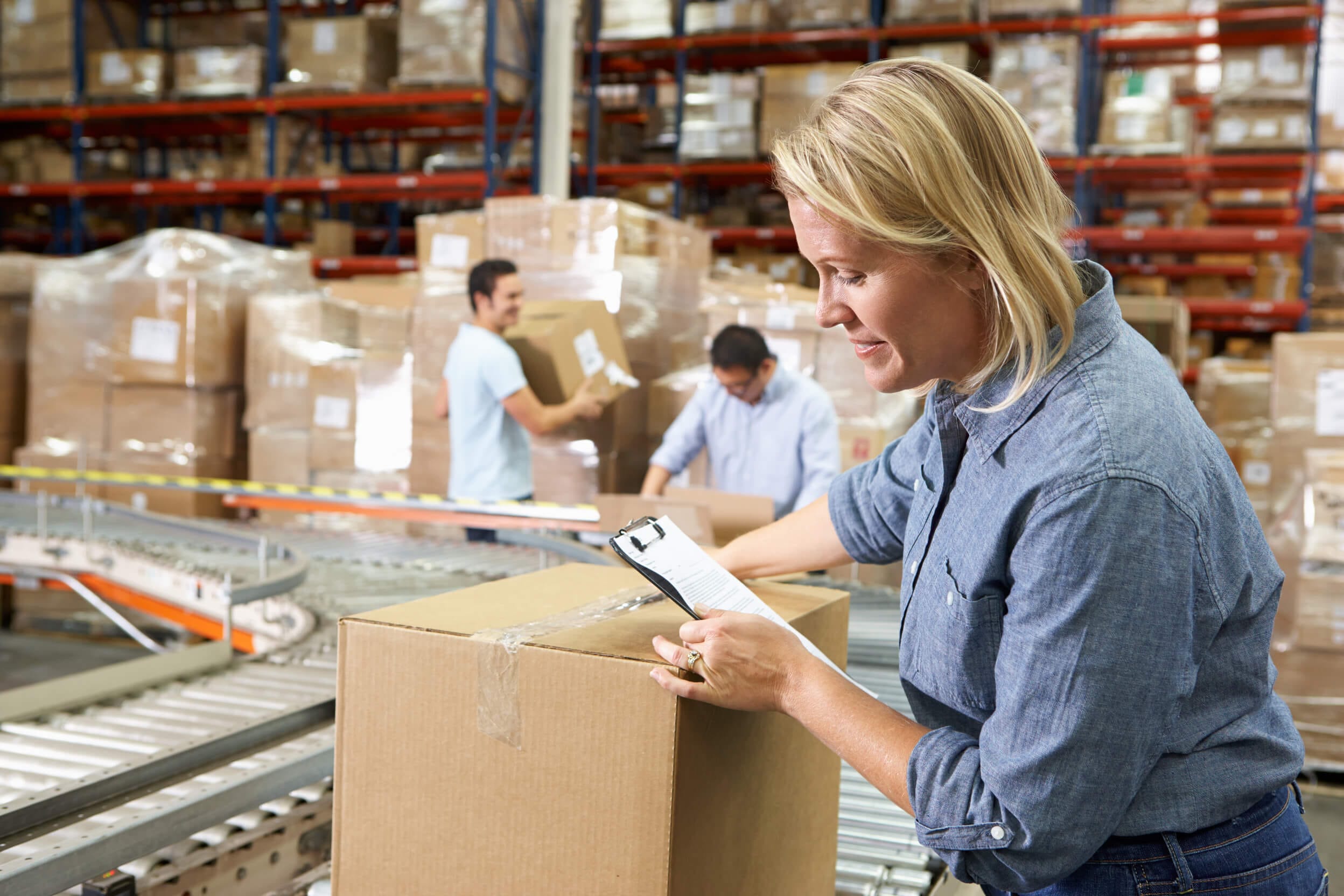 A team of warehouse workers loading and checking boxes on a conveyer belt.