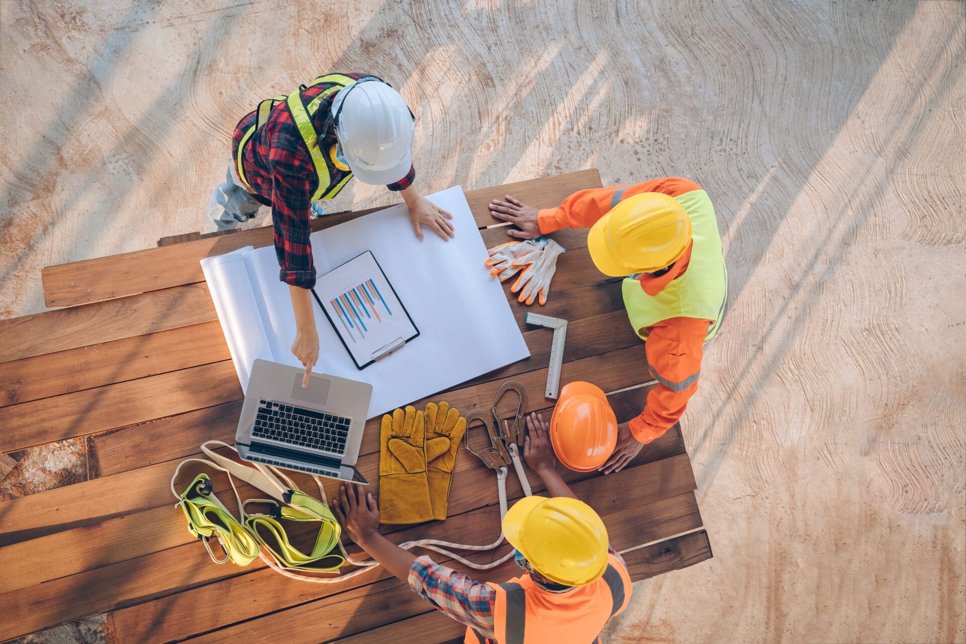 Construction workers in safety gear collaborating on a project with a laptop and blueprints, showcasing teamwork and adaptability in workforce management.