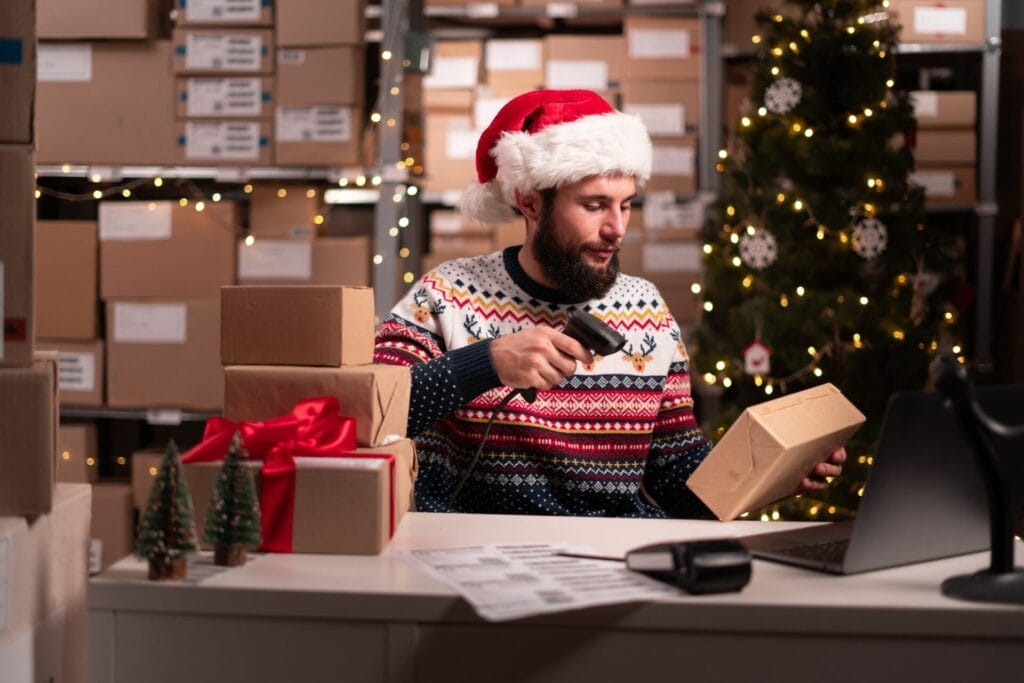 Warehouse worker wearing a festive Santa hat, scanning packages during the holiday season, illustrating the importance of on-demand seasonal work and efficient business operations.