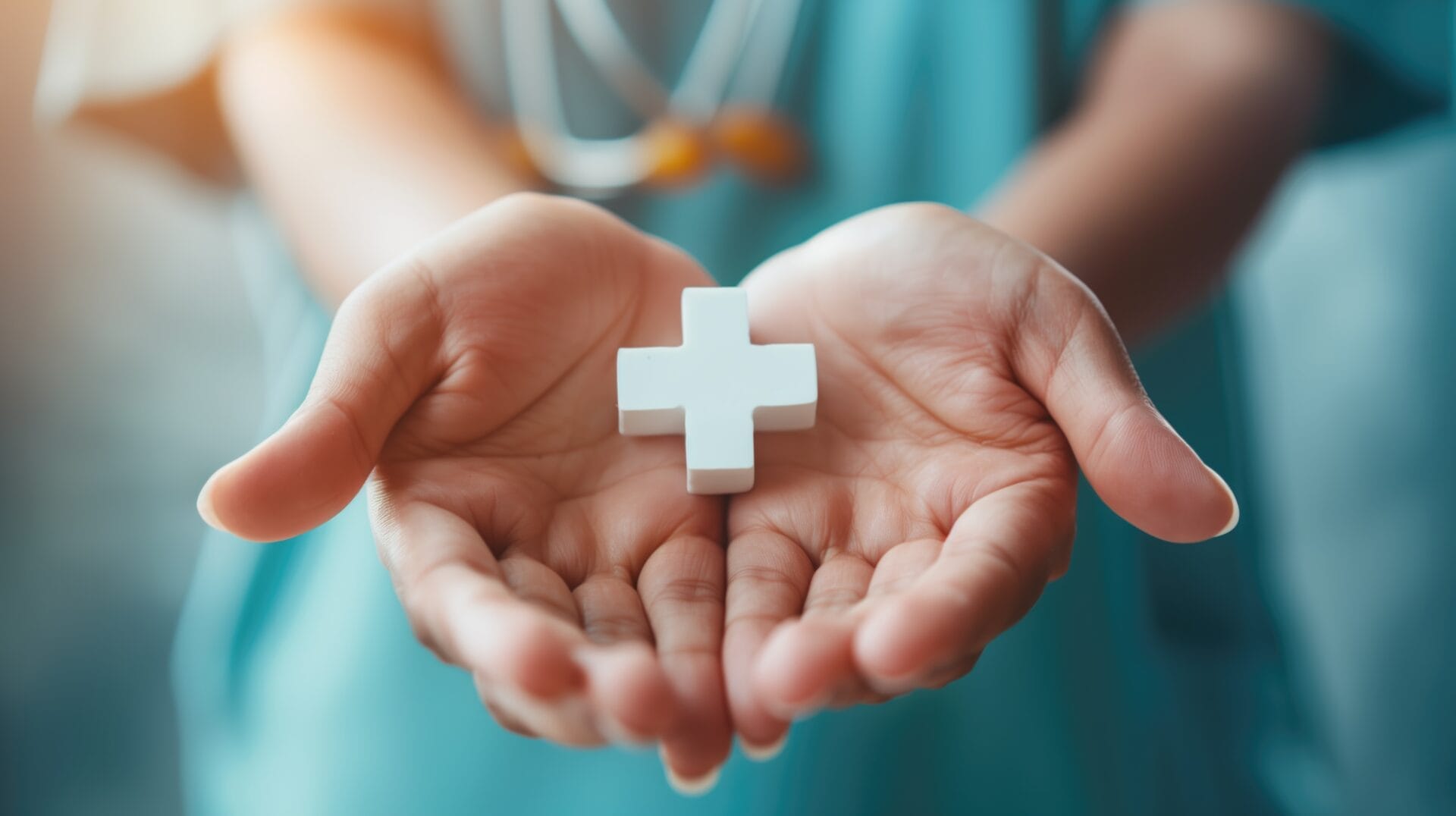 Close-up of hands holding a white medical cross symbol, representing healthcare and protection.